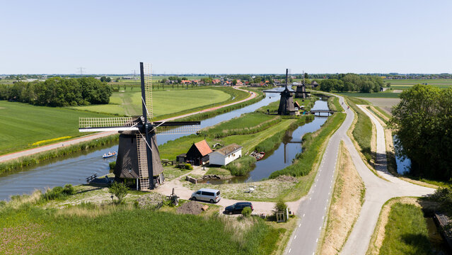 Aerial view of the historic Strijkmolen K windmill and other traditional mills along a canal surrounded by green fields in Oterleek, Noord-Holland, Netherlands.