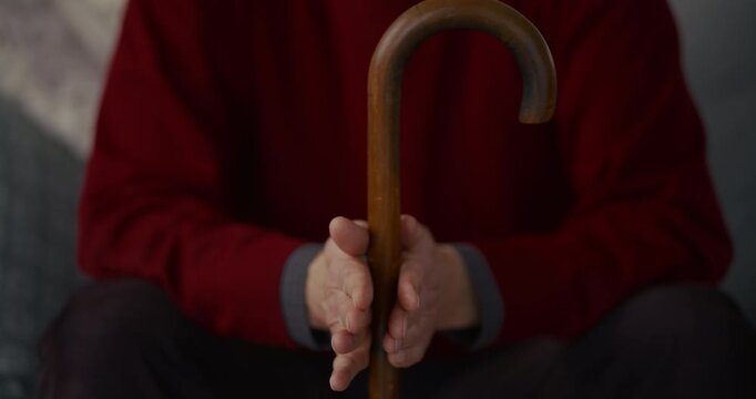 Elderly person holding a wooden cane while seated indoors