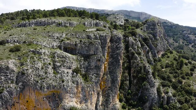 Aerial view of a dramatic rocky ridge with steep cliffs and dense Mediterranean pine forest on western slopes within rugged mountainous Sierra Aitana, Spain. 