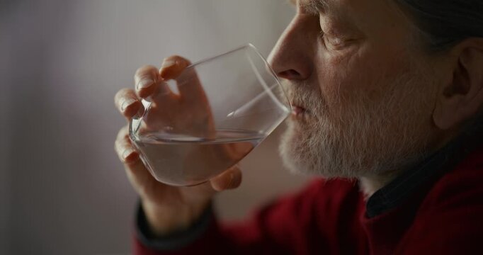 Elderly bearded man drinking water indoors in soft natural light