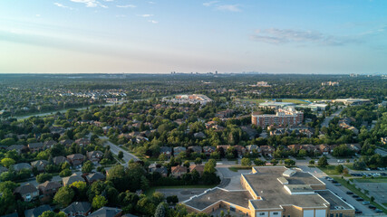 Naklejka premium An expansive, high-angle aerial drone photograph looking across a green residential Oakville neighborhood with a public school in the foreground toward the distant Toronto and Mississauga skylines.