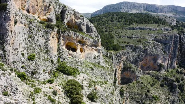 Aerial view of a dramatic rocky ridge with steep cliffs and dense Mediterranean pine forest on western slopes within rugged mountainous Sierra Aitana, Spain. 
