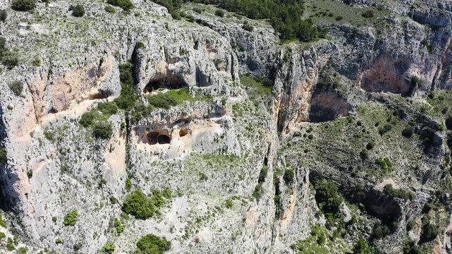 Aerial view of a dramatic rocky ridge with steep cliffs and dense Mediterranean pine forest on western slopes within rugged mountainous Sierra Aitana, Spain. 