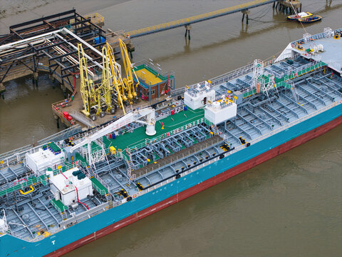Aerial view of a large industrial tanker ship docked at a terminal with yellow loading arms on the River Thames in London, Greater London, United Kingdom.