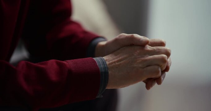 Clasped hands in a red sweater by a window in soft daylight