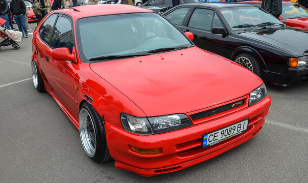 Bright red Toyota Corolla (E100) hatchback with a lowered stance and deep dish silver wheels represents a classic 90s icon within the modern tuning scene