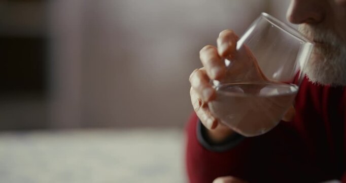 Hand Near Clear Drinking Glass on Patterned Tablecloth in Soft Indoor Light