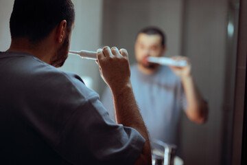 Unrecognizable Man Brushing Teeth With Electric Toothbrush In Bathroom Mirror. Anonymous male...