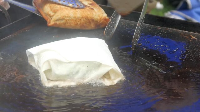 a person's hands cooking square shaped egg martabak and burger patty meat on a hot flat pan