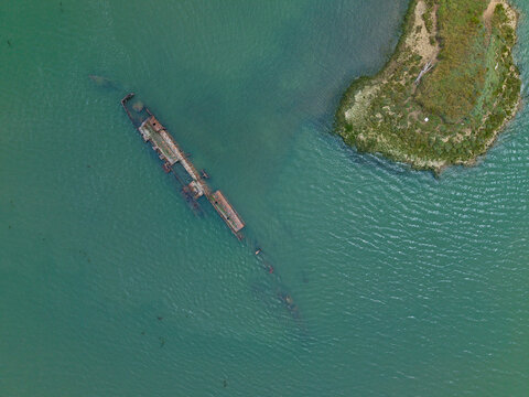 Aerial view of the rusted remains of the German Submarine shipwreck lying in the shallow green waters of the estuary near a grassy bank in River Medway, Kent, United Kingdom.