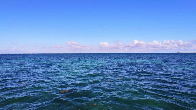 4K aerial drone shot flying low over the turquoise Caribbean sea in Punta Sam, Mexico. Cinematic low altitude water skimming view with blue sky and ocean horizon.