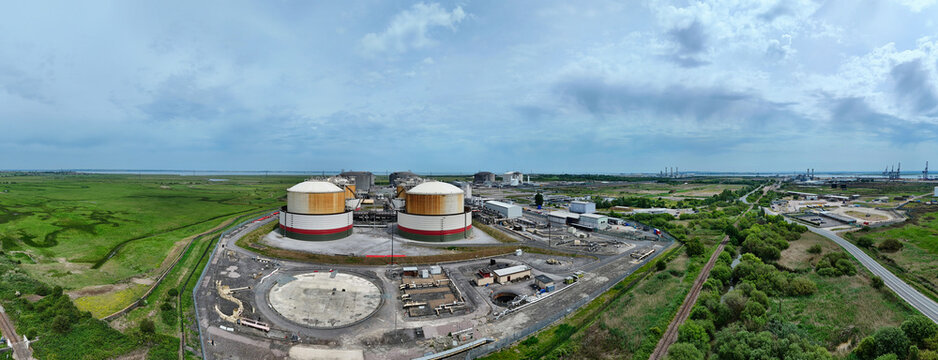 Aerial view of the Grain LNG terminal featuring large storage tanks and industrial infrastructure surrounded by green fields under a cloudy sky Wallend, England, United Kingdom.