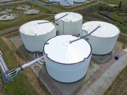 Aerial view of Grain LNG storage tanks with white roofs, industrial pipelines, and surrounding green fields in Wallend, England, United Kingdom.