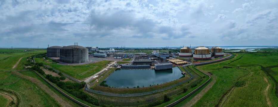 Aerial view of Grain LNG terminal featuring massive storage tanks, industrial infrastructure, and surrounding green marshlands under a cloudy sky Wallend, England, United Kingdom.