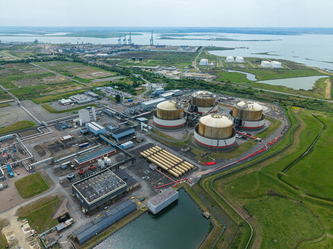Aerial view of the Grain LNG terminal featuring large circular storage tanks and industrial infrastructure surrounded by green fields in Wallend, England, United Kingdom.
