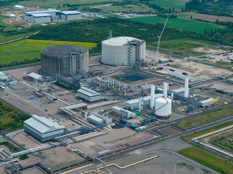 Aerial view of the Grain LNG terminal featuring massive storage tanks and complex industrial infrastructure surrounded by green fields in Wallend, England, United Kingdom.