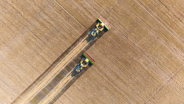 This aerial overhead shot captures two trains traveling along parallel railway tracks through a large, neatly cultivated farm field.