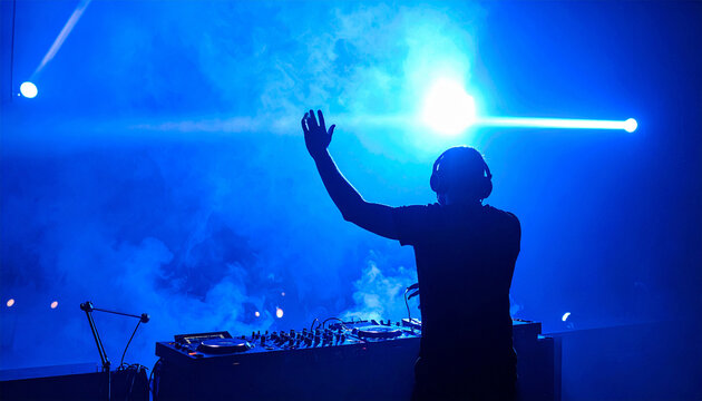 DJ's Electrifying Performance: A silhouette of a DJ, immersed in the vibrant blue light of the stage, commands the crowd with a raised hand, surrounded by fog and illuminating spotlights.