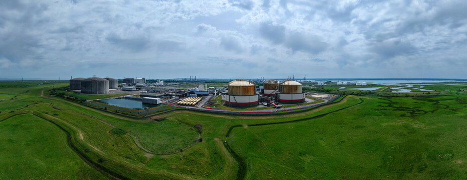 Aerial view of the Grain LNG terminal with large storage tanks and industrial infrastructure surrounded by green fields and coastal marshes in Wallend, England, United Kingdom.