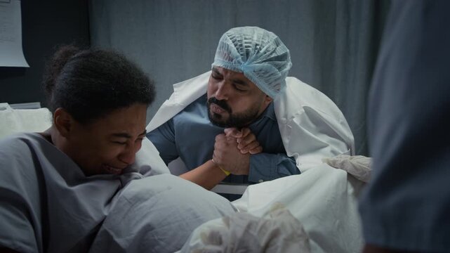 Black pregnant woman pushing and giving birth in hospital bed while husband holds her hand. Footage is ideal for maternity clinic advertising and childbirth education