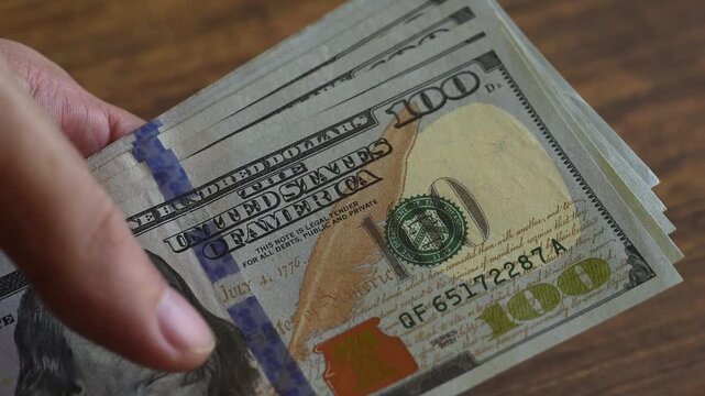 Close-up of hands counting one-hundred-dollar bills.