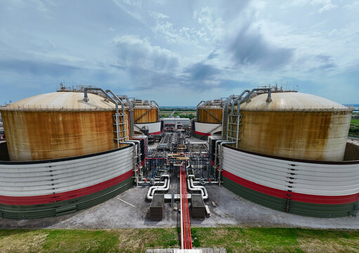 Aerial view of Grain LNG storage tanks and industrial infrastructure with complex piping systems and green fields under a cloudy sky in Wallend, England, United Kingdom.