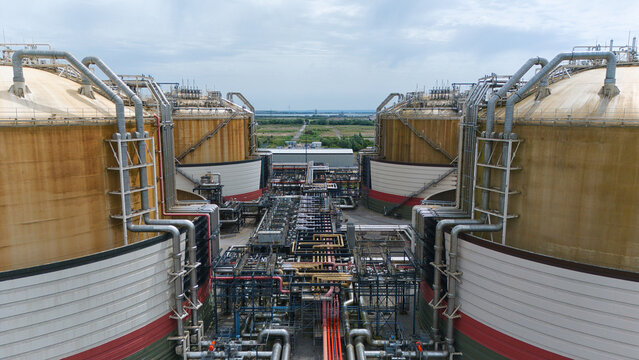 Aerial view of Grain LNG terminal featuring massive storage tanks and intricate industrial piping under a cloudy sky Wallend, England, United Kingdom.