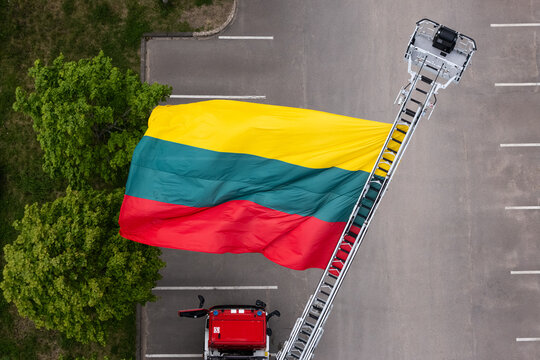 Aerial view of a large Lithuanian flag displayed on a fire truck ladder over an empty parking lot next to green trees in Vilnius, Vilnius County, Lithuania.