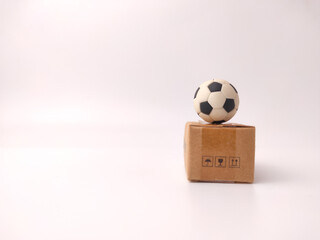 A miniature black and white soccer ball is balanced on top of a small, brown cardboard parcel box