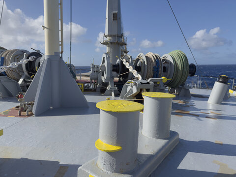 Anchor handling and mooring equipment on cargo ship forecastle. Anchor chain runs from deck opening through stopper to windlass wildcat and into chain locker. Mooring winch with coiled hawser