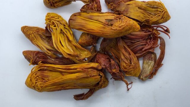 pile of dried Rampatri (Wild Mace) pieces isolated on a clean white background. The image showcases the intricate, reticulated, and lacy texture of these orange-brown whole spices. 