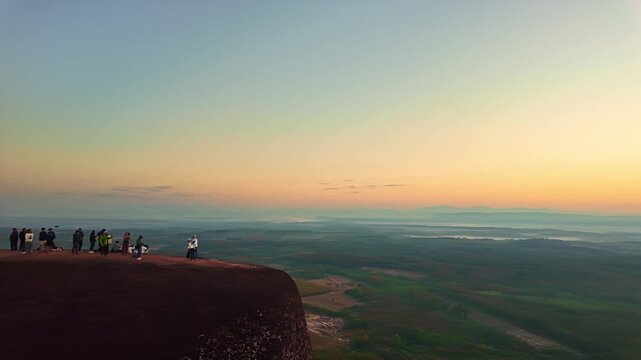 Travelers explore the iconic Three Whale Rock during sunrise as warm sunlight illuminates the rugged cliff landscape and panoramic countryside views of Isan, Thailand. Hin Sam Wan viewpoint