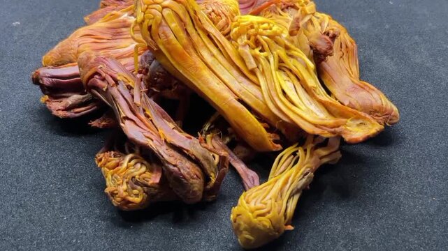 pile of dried Rampatri (Wild Mace) pieces isolated on a clean black background. The image showcases the intricate, reticulated, and lacy texture of these orange-brown whole spices. 