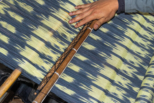 A close-up of man's hands working on a macana shawl using the ikat technique on a belt loom. This is a cultural heritage of Ecuador. Azuay provine, Gualaceo