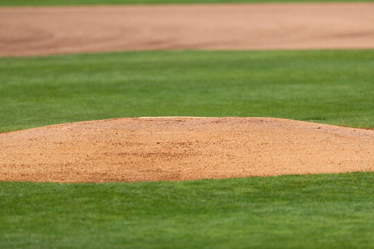 Pitchers mound on a high school baseball field surround by freshly mowed green grass. The mound of red clay dirt has just been prepared for game play.