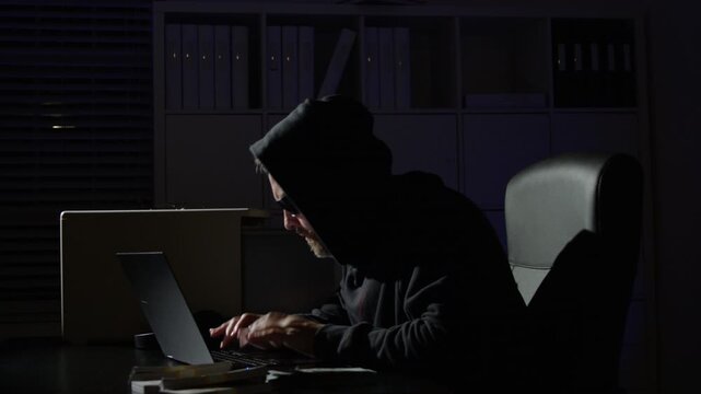 Office hacker typing malware at night. Digital hacker attack threatens IT systems. Cybercrime hacker risks online privacy. Network hacker breach causes security threat.