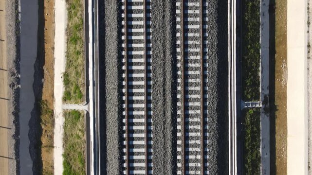 Aerial view of parallel railway tracks with grey gravel ballast and concrete sleepers surrounded by green vegetation in Desenzano del Garda, Lombardy, Italy.