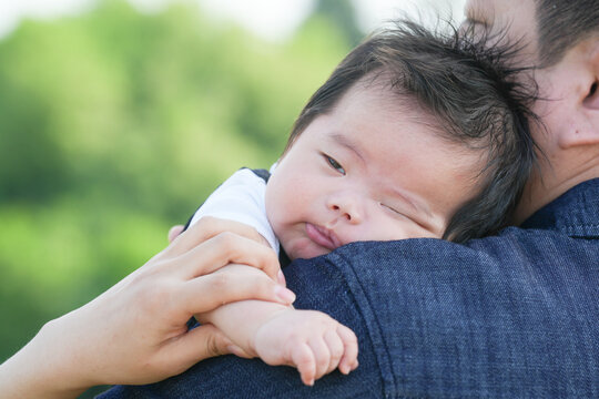 Soft light bathes a sleeping infant nestled in arms. Child's eyes close, face relaxed, fingers curled gently. Parent holds baby close, offering calm, protective comfort