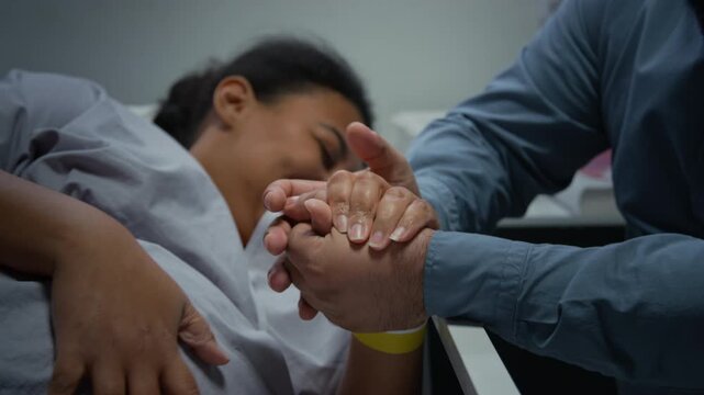Pregnant woman in labor grimacing in pain with husband holding her hand in hospital maternity ward. Footage is perfect for healthcare marketing and childbirth education campaigns, close up