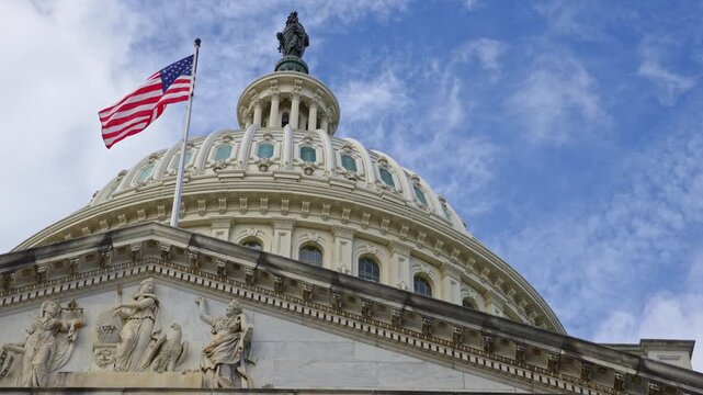 American flag waving on Capitol landmark. American flag in clouds. American flag for patriotism symbol. American flag on government facade.