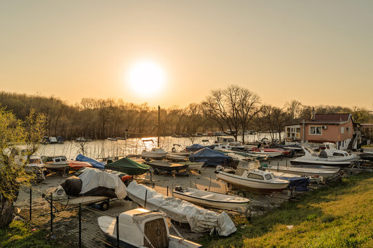 Boats are moored and stored along the bank of the Tamis or Timis River on Tamiski Kej in Pancevo, Serbia, with evening sunlight and a quiet marina setting.