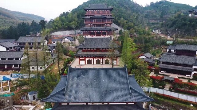 Aerial view of a multi tiered ancient Chinese temple complex built along a green mountain slope in China. Buildings with dark tiled roofs follow the terrain creating a dramatic cascading architectural