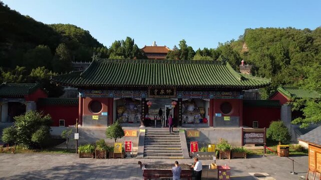 Aerial view of a historic Chinese temple in China distinguished by rare green glazed roof tiles, surrounded by autumn colored foliage and evergreen pines. Captures seasonal beauty alongside classic wo