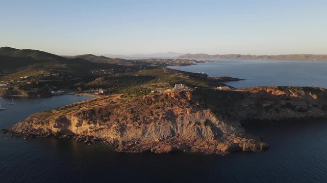 Aerial view of the Archaeological Site of Sounion on a rocky cliff overlooking the Aegean Sea during golden hour in East Attica Regional Unit, Greece.