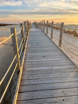 Wooden boardwalk path leading through sand dunes to the beach at Labenne Ocean in Landes, France. Coastal walkway with rope railings under a beautiful sunset sky