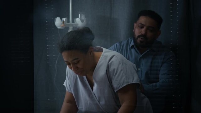 Pregnant woman leaning on hospital bed rail,breathing through painful labor contractions while husband supporting her. Clip is suitable for maternity care and childbirth education videos