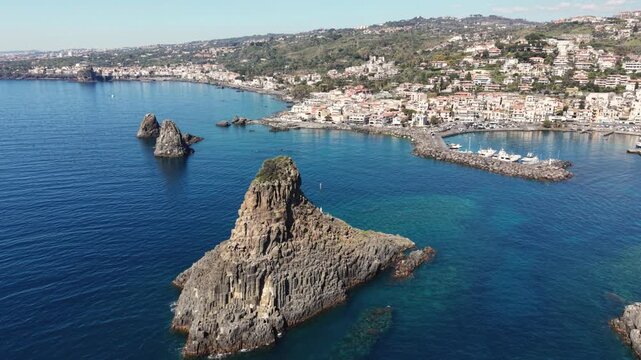 Aerial view of the volcanic Islands of the Cyclops rising from the blue sea near the coastal town and harbor of Aci Castello, Catania, Italy.