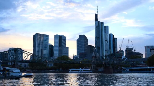 Frankfurt skyline along Main river with Eiserner Steg bridge during sunset.