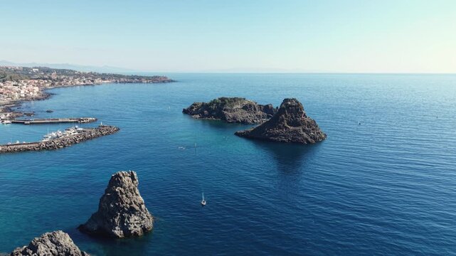 Aerial view of the Islands of the Cyclops rising from the blue Mediterranean Sea near the harbor and coastline in Aci Castello, Catania, Italy.