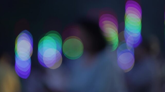 Close up colorful illumination bokeh background with blurred silhouettes of people walking past neon light decorations at night temple festival fair.